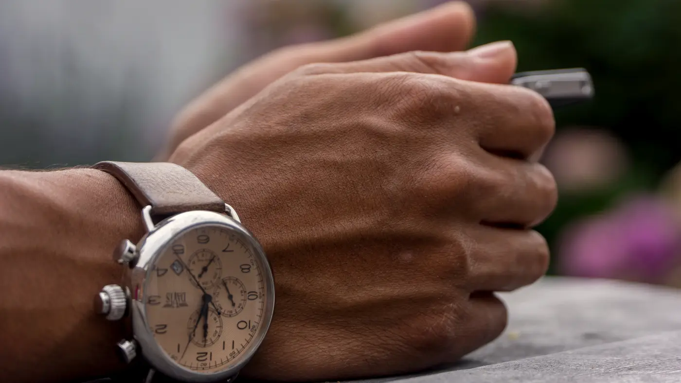 Man's wrist with a chronograph watch while holding a pen