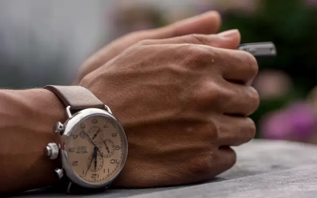 Man's wrist with a chronograph watch while holding a pen