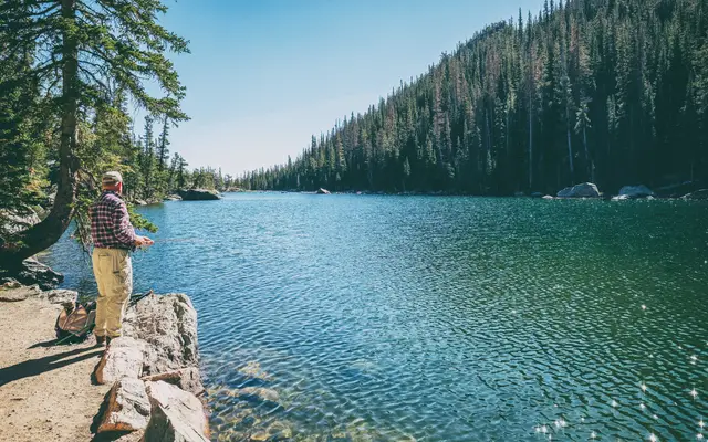 Older man fishing from the rocky shore of a mountain lake