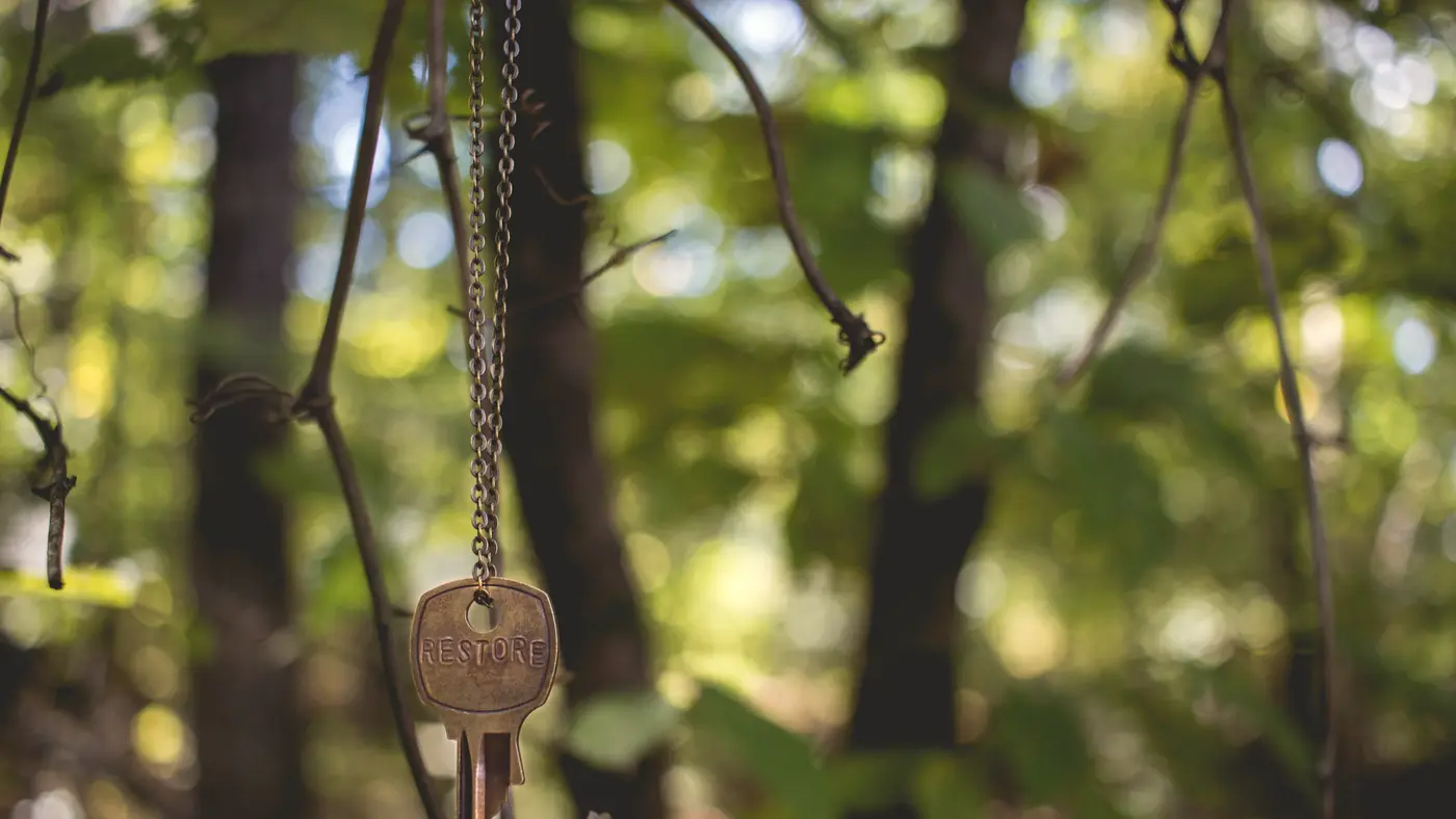 Old brass key hanging from a string in a sunlit forest