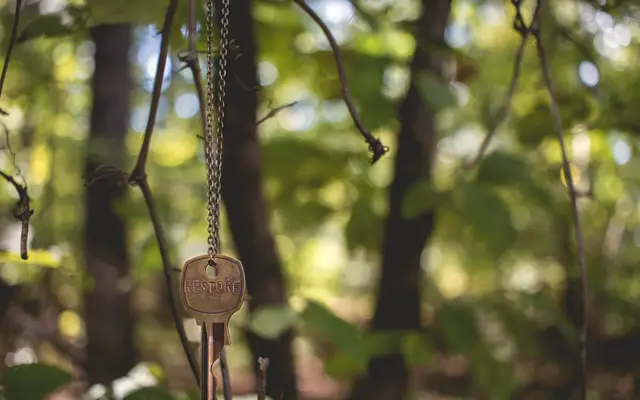 Old brass key hanging from a string in a sunlit forest