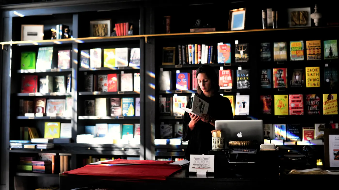 Bookshop worker reading at the counter among full shelves