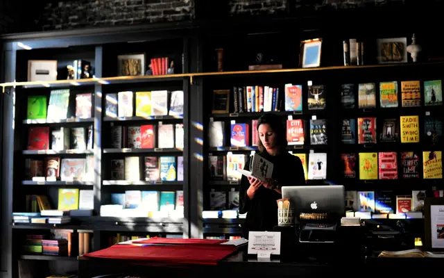 Bookshop worker reading at the counter among full shelves