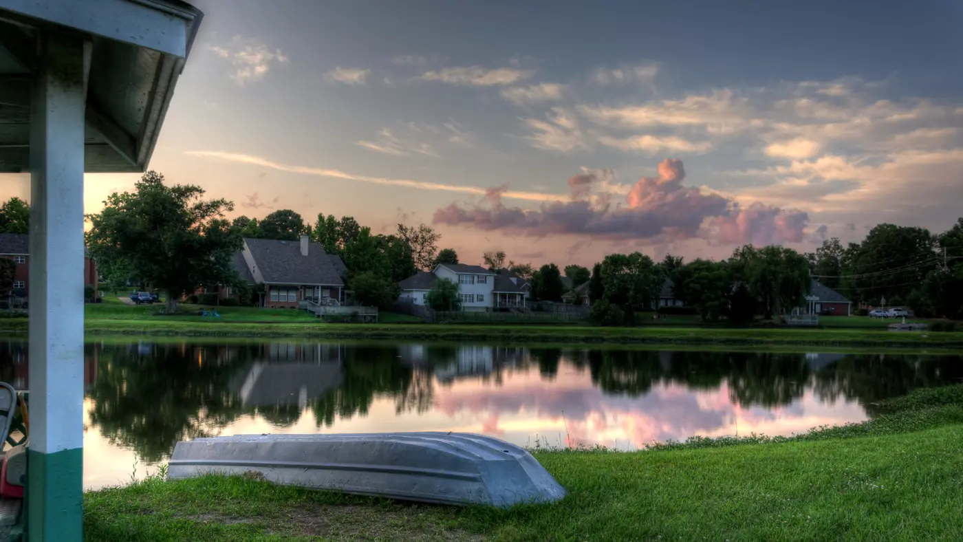 Rowboat on a lawn beside a quiet pond at sunset