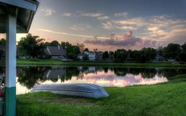 Rowboat on a lawn beside a quiet pond at sunset