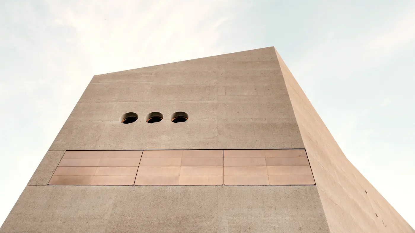 Sandstone tower with three small round windows against a pale sky