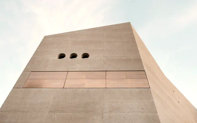Sandstone tower with three small round windows against a pale sky