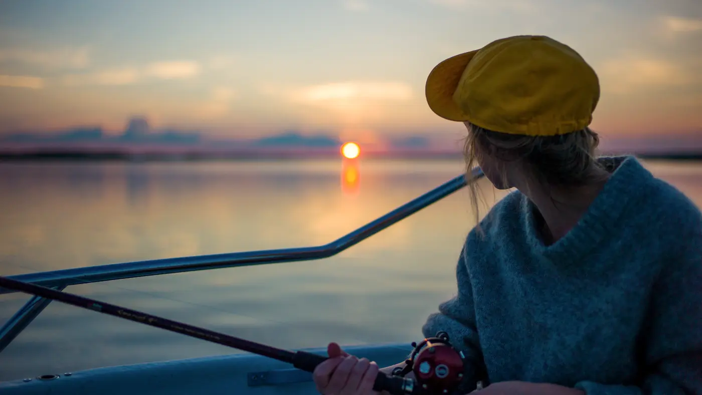 Woman fishing from a boat as the sun sets over water
