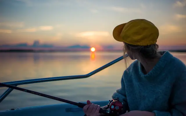 Woman fishing from a boat as the sun sets over water