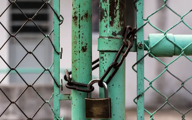 Padlock and chain securing a green chain-link gate