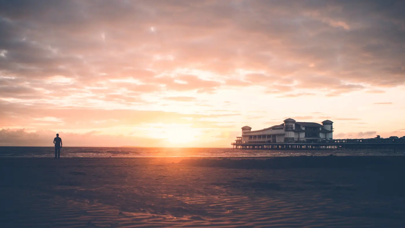 Lone figure on a wide beach watching a calm sunset