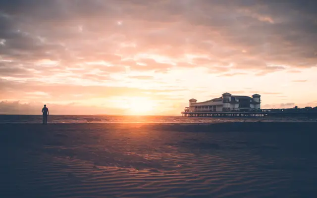 Lone figure on a wide beach watching a calm sunset
