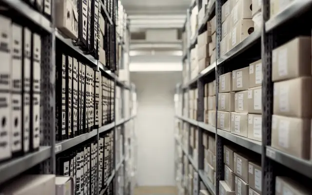 Narrow aisle between tall steel shelves stacked with storage boxes