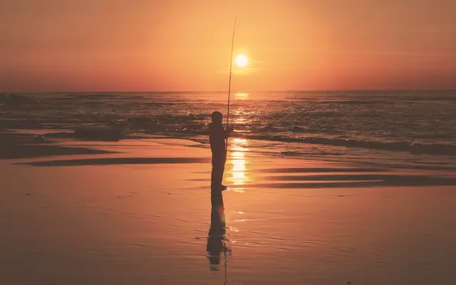 Angler casting into the surf at an orange sunset