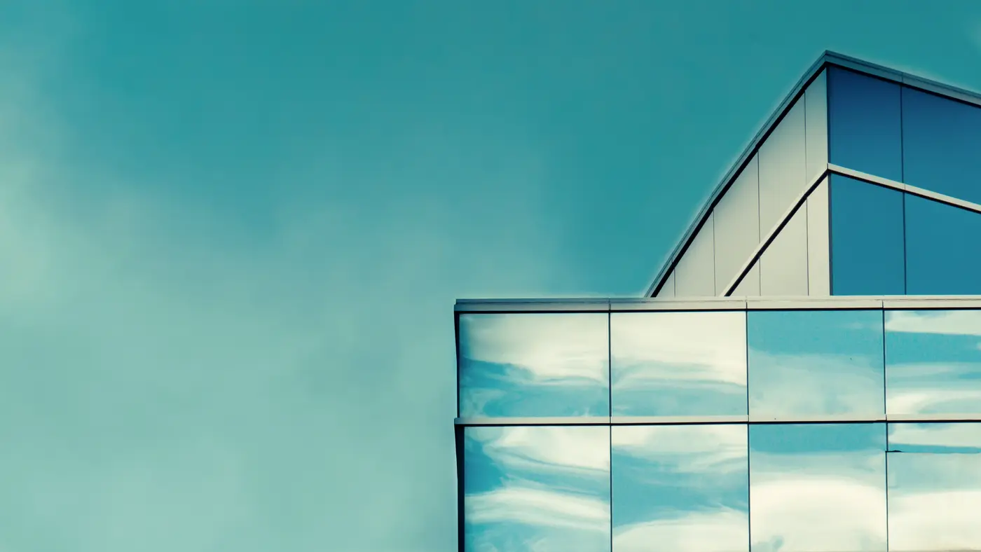 Corner of a glass office building reflecting a clear blue sky