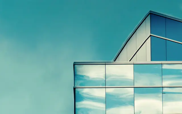 Corner of a glass office building reflecting a clear blue sky