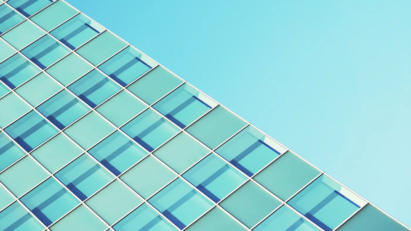 Blue glass office tower facade rising diagonally against clear sky