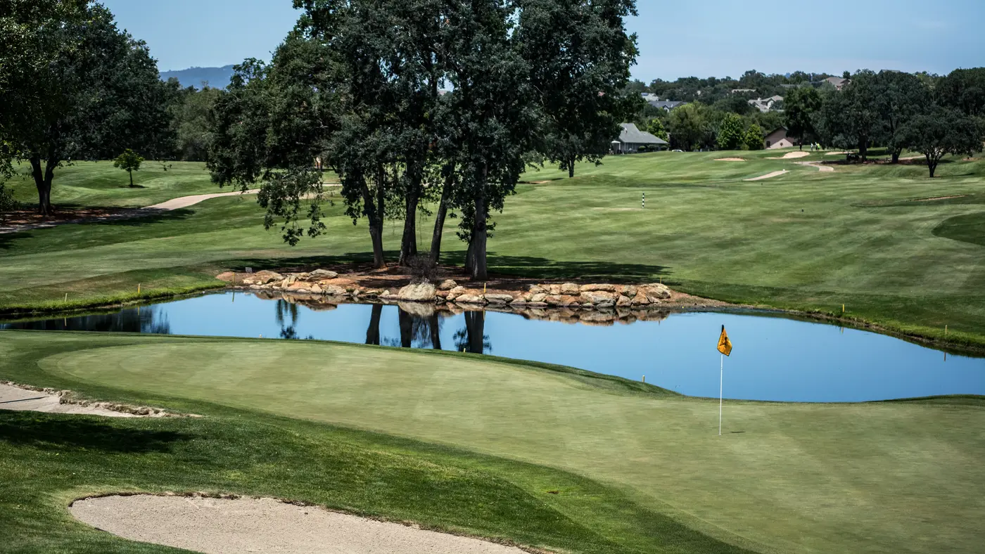 Golf course green with a pond and oak trees