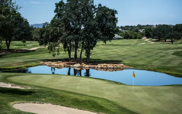 Golf course green with a pond and oak trees