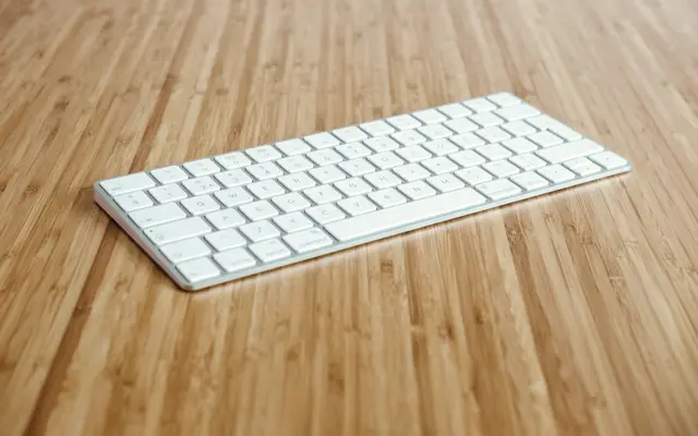 White wireless keyboard on a light bamboo desk