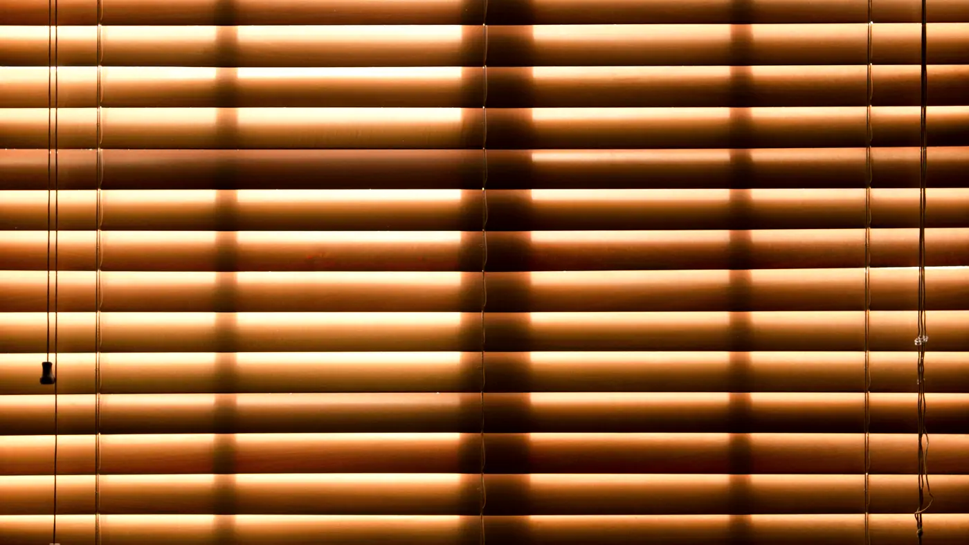 Closed window blinds glowing with warm light