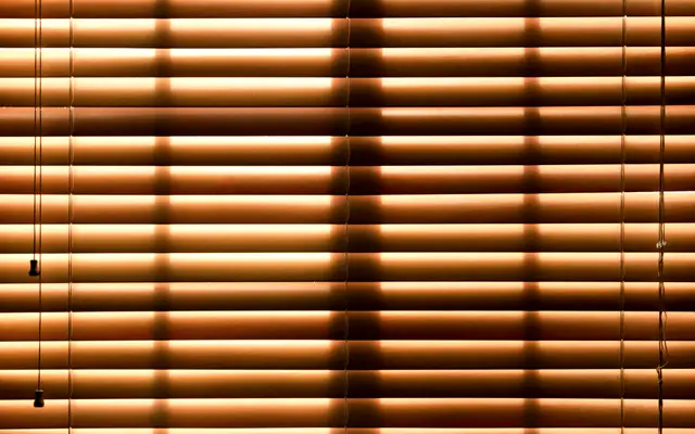 Closed window blinds glowing with warm light