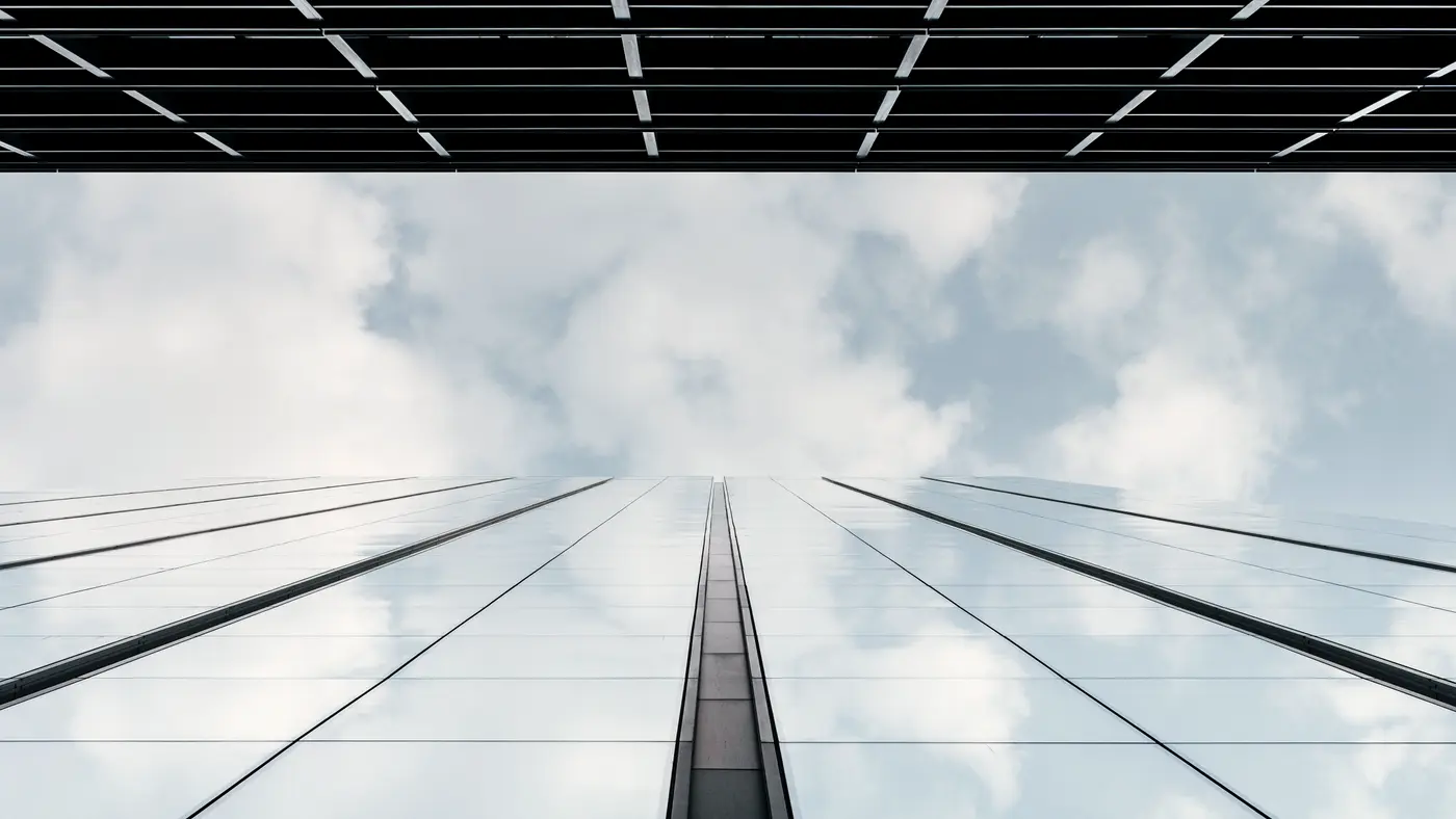Looking up a glass skyscraper reflecting soft white clouds