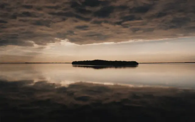 Calm lake with a small island reflecting a cloudy dusk sky
