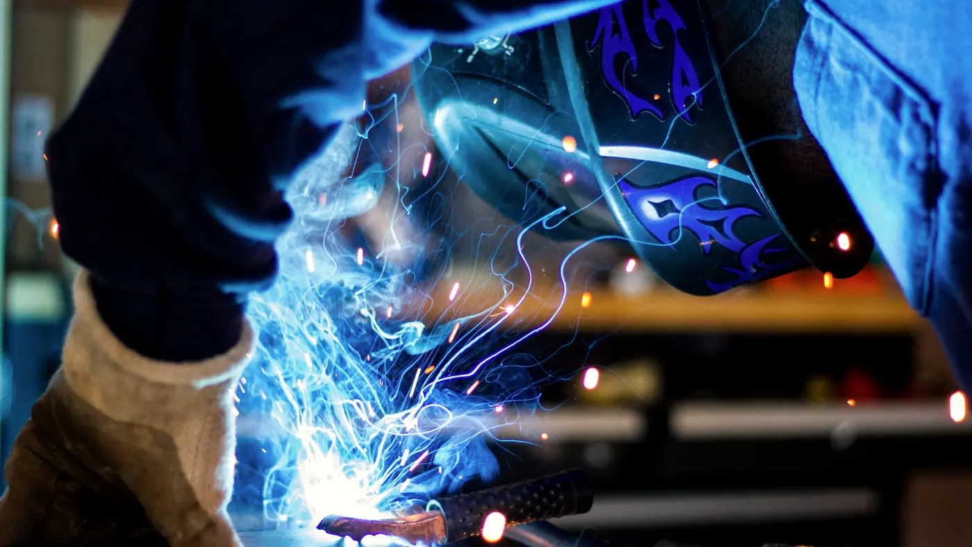 Welder in helmet and gloves working as sparks fly