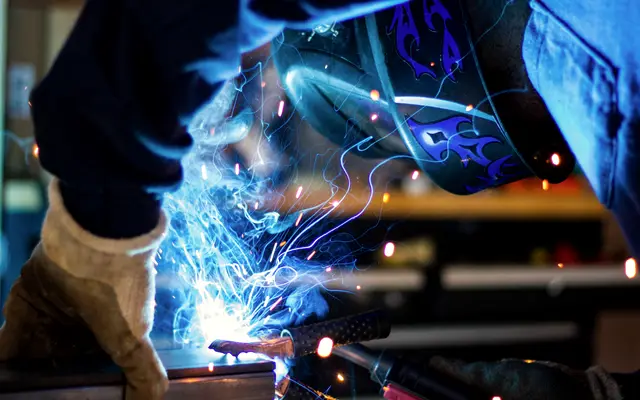 Welder in helmet and gloves working as sparks fly