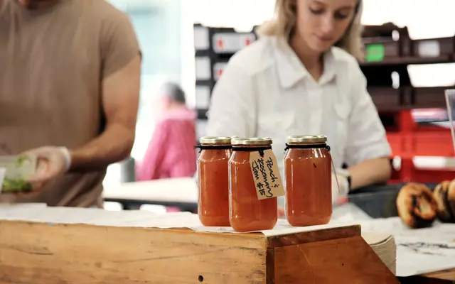 Market stall vendor arranging jars of homemade preserves