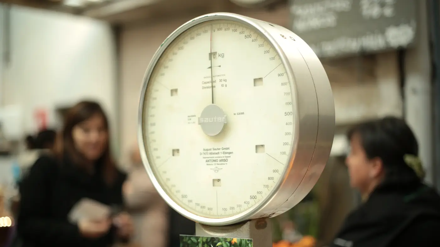 Old dial scale at a market stall with shoppers behind