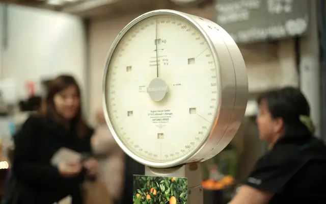 Old dial scale at a market stall with shoppers behind