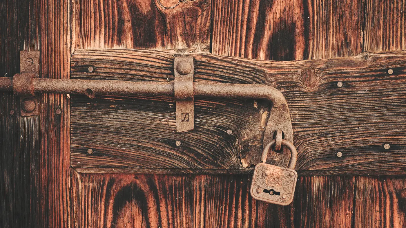 Old padlock on an iron latch of a weathered wooden door