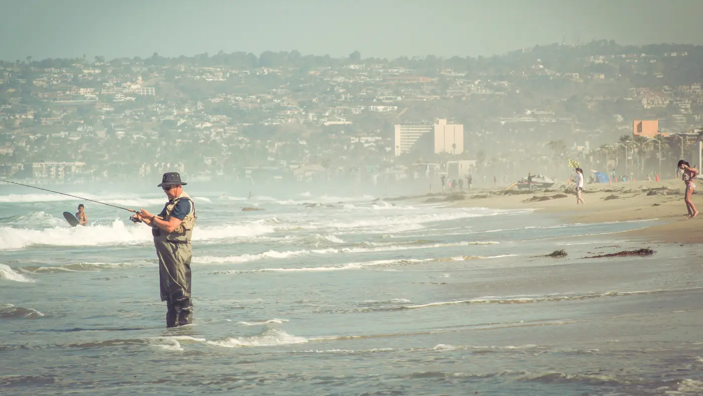 Older man surf fishing on a hazy coastal beach