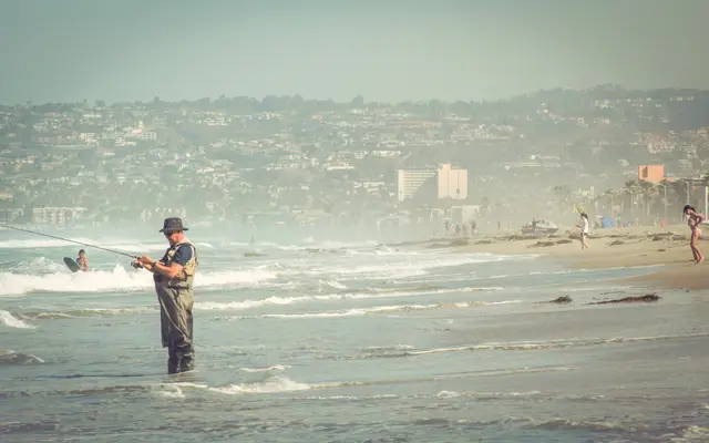 Older man surf fishing on a hazy coastal beach