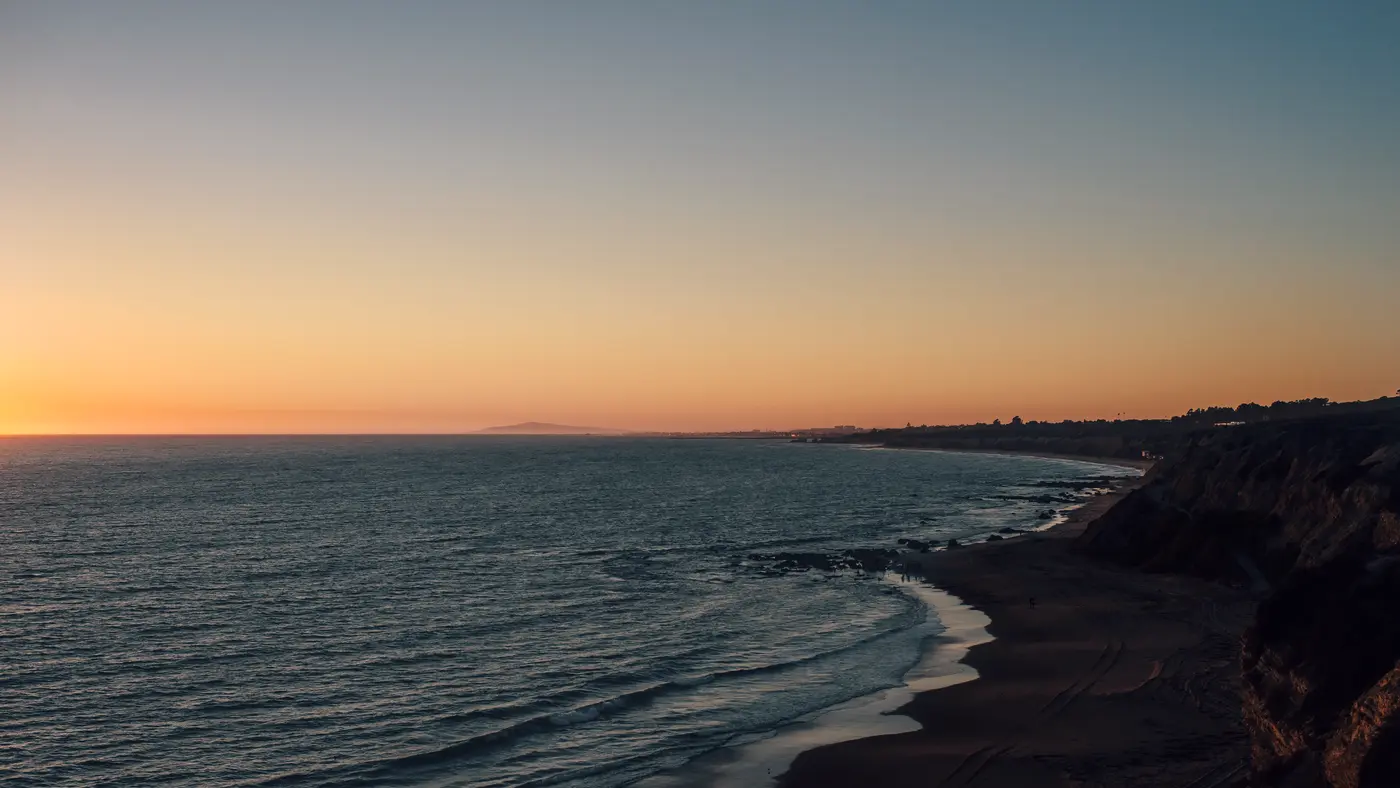 Quiet coastline and bluffs at dusk under a clear orange sky