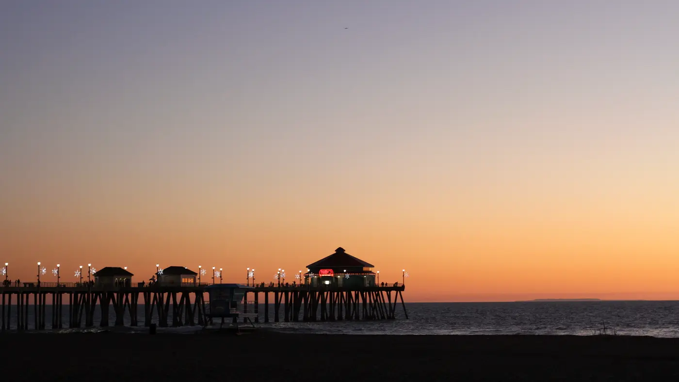 Long pier silhouetted against a calm orange sunset sky