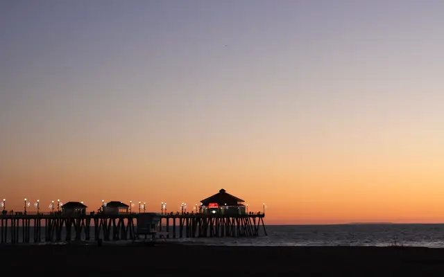 Long pier silhouetted against a calm orange sunset sky