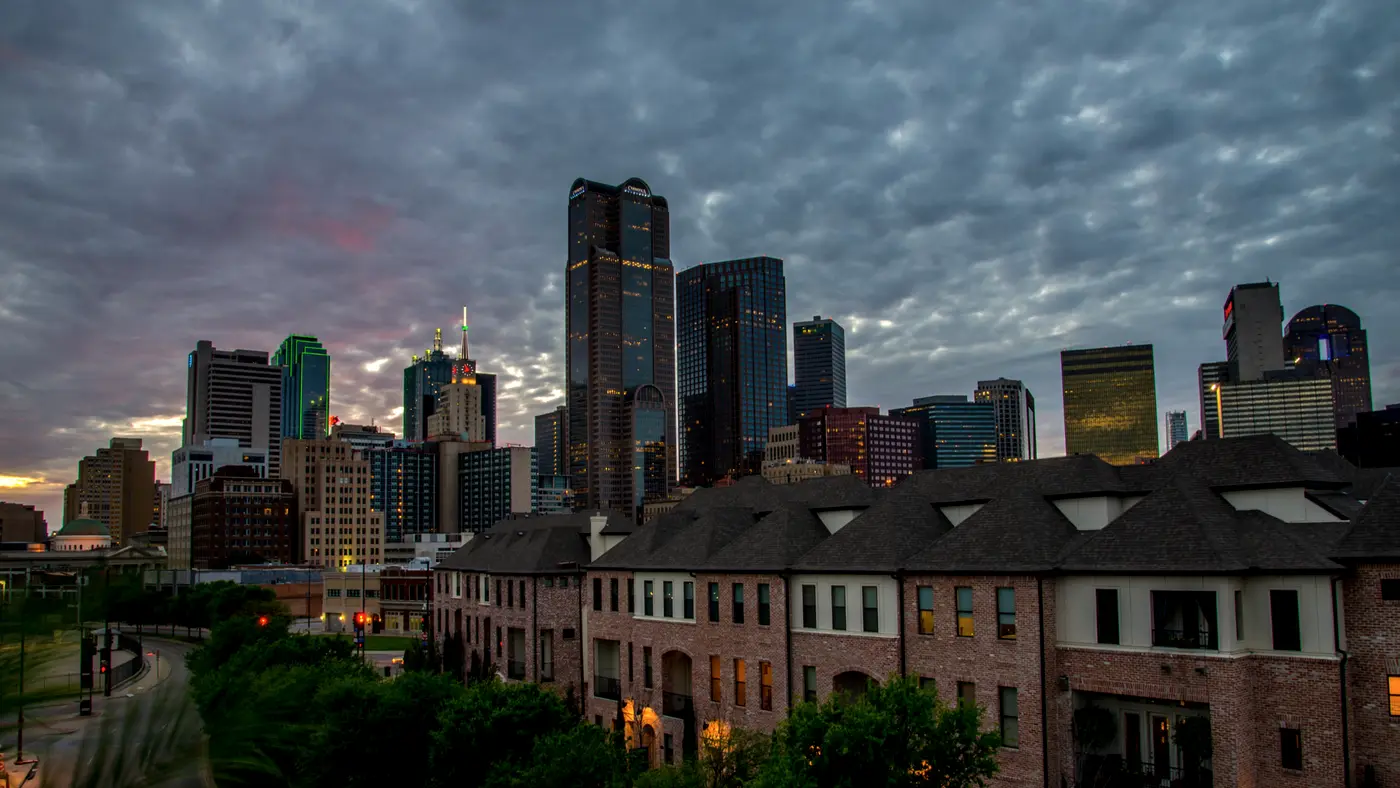 Dallas skyline behind townhouses under a dramatic cloudy sky