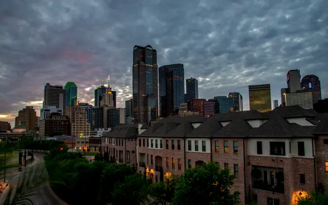 Dallas skyline behind townhouses under a dramatic cloudy sky