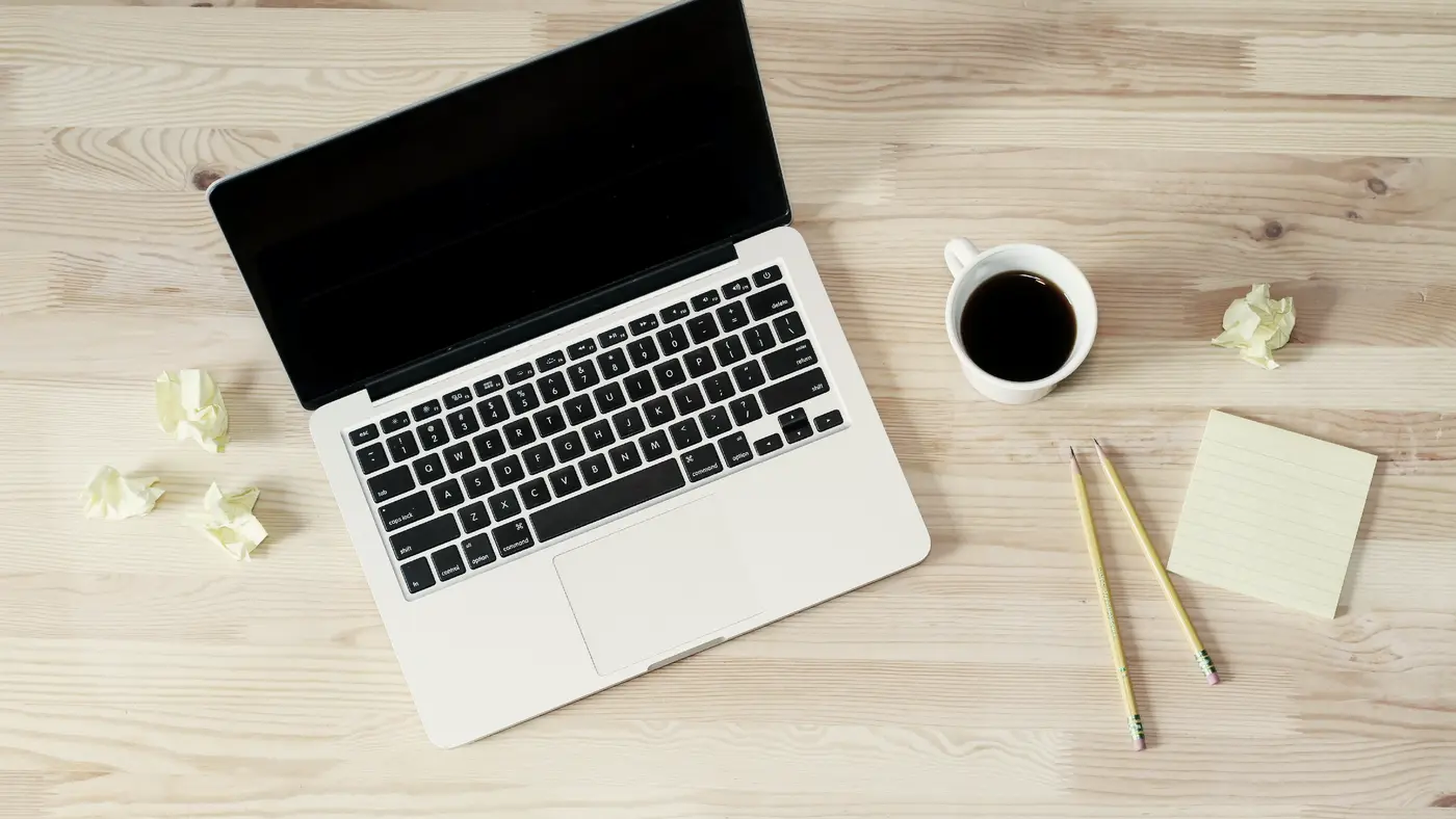 Laptop, black coffee and pencils on a pale wooden desk