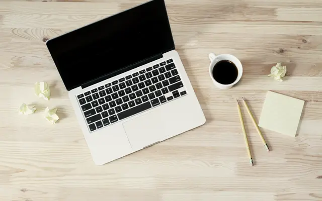 Laptop, black coffee and pencils on a pale wooden desk