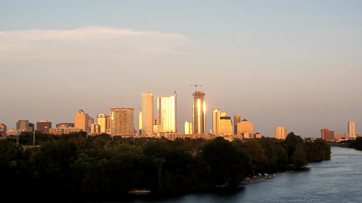 Austin skyline glowing in golden light beyond the river and trees